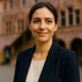 Portrait d'une femme en blazer devant un bâtiment historique.